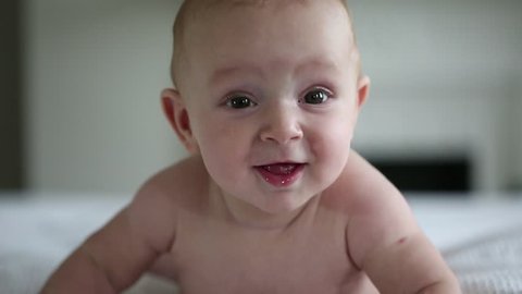 Beautiful Smiling Baby: A gorgeous little baby lies on the bed and smiles at the camera with a nice soft focus background. 