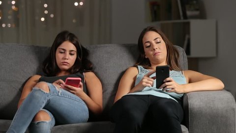 Bored antisocial friends ignoring each other using their phones sitting on a couch in the living room at home