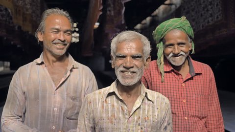 Mid shot of Laborers or old men working in the textile printing industry smiling. Three happy elderly daily wage workers laughing in front of the camera standing in the bed sheet printing factory
