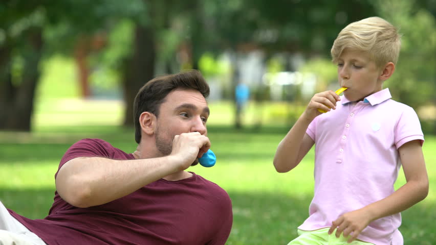 Father and son blowing up balloons, having fun together, carefree recreation
