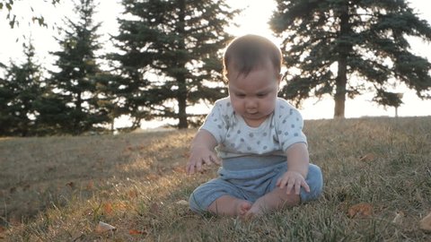 Small baby girl sitting on grass in park. Beautiful infant baby girl portrait in nature