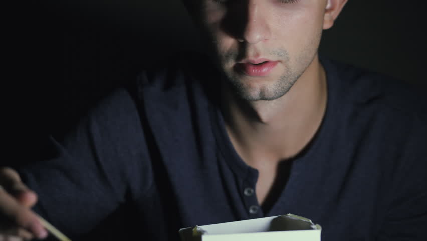 Close-up of a man who is eating noodles with chopsticks from a box. European man eating Chinese food