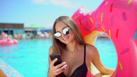 Beautiful young bikini woman in pool on beach with smartphone. Bikini girl in pool using, texting on mobile phone. traveler woman smiling tourism happy holiday beauty vacation summertime summer time