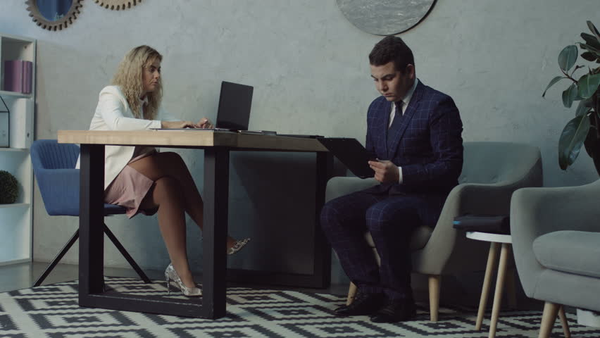 Concentrated male job applicant completing employment application form at office while pretty hr recruiter working at her desk. Serious job seeker filling out application form for new vacancy. | Shutterstock HD Video #1017840535