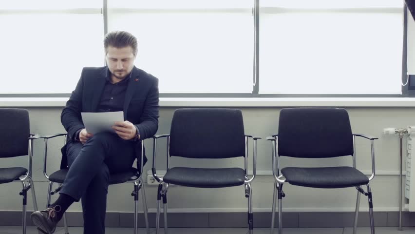 Ready for interview thoughtful man in formal wear holding paper while sitting at the chair in office hall. Businessman sitting on chair while waiting in airport room and viewing documents. Royalty-Free Stock Footage #1017842884