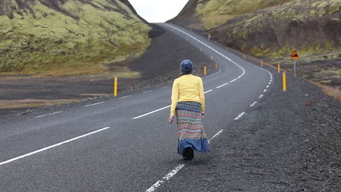 A young woman walks and runs along the road in the mountains. She is happy, happy, admiring and having fun with delight. Iceland