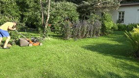 young man work with grass cutter in own green flower garden near home. 4K UHD video clip.