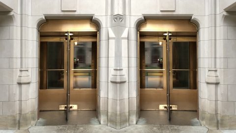 A lopping shot of two golden revolving glass doors in a stone building.	