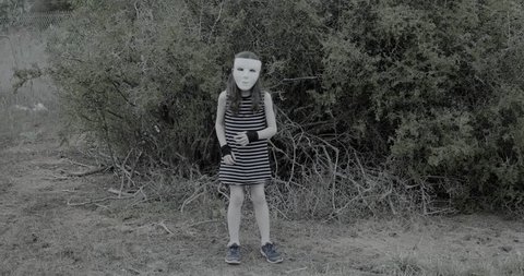 young girl wearing a white halloween mask stands spookily and then runs in scary manner towards the camera