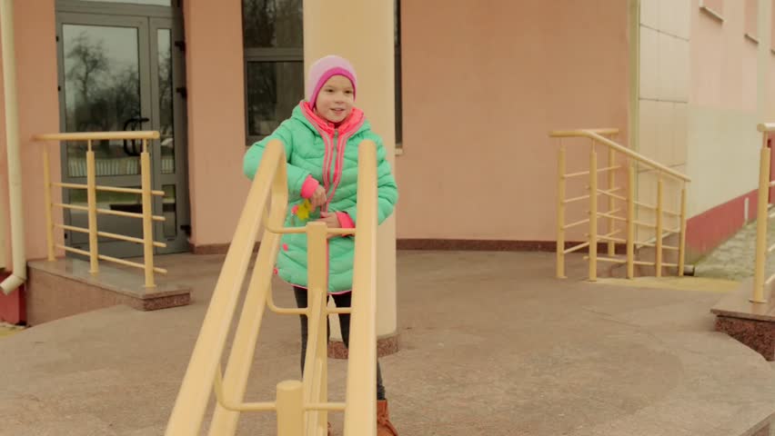 Little beautiful girl in an autumn jacket climbs on metal railing near building