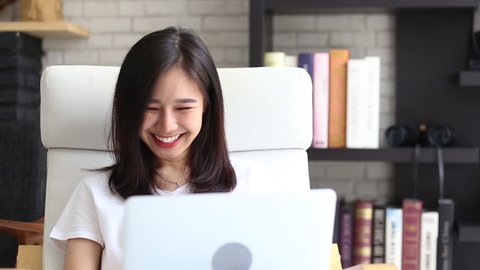Beautiful of portrait asian young woman working online laptop with smile and happy and laughing sitting at living room, girl using notebook compute, business and success concept.