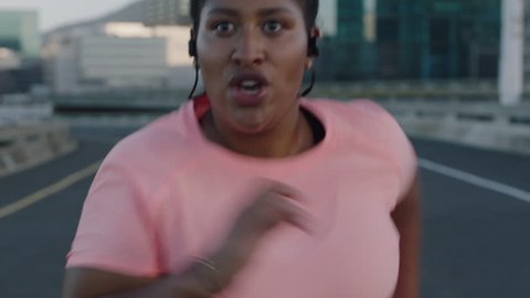overweight african american woman runner exercising running difficult weight loss challenge jogging in urban city at sunset wearing earphones