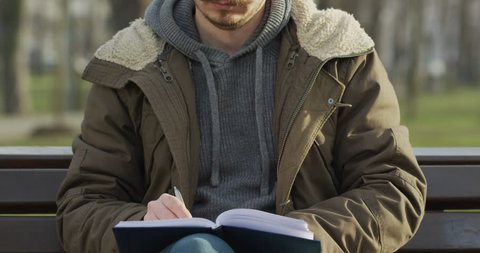 Man sitting on a bench and writing in a notebook.