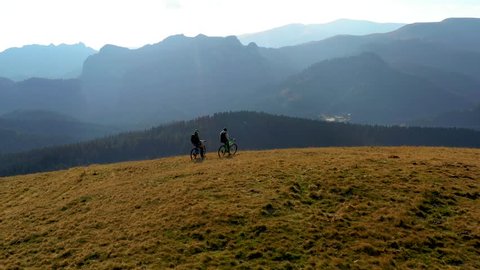 Aerial view. Epic shot of a mountain bikers on top of the mountain looking down the valley. Aerial shot of mountain bikers on the top looking at amazing view in the autumn. Tracking shot of friends 