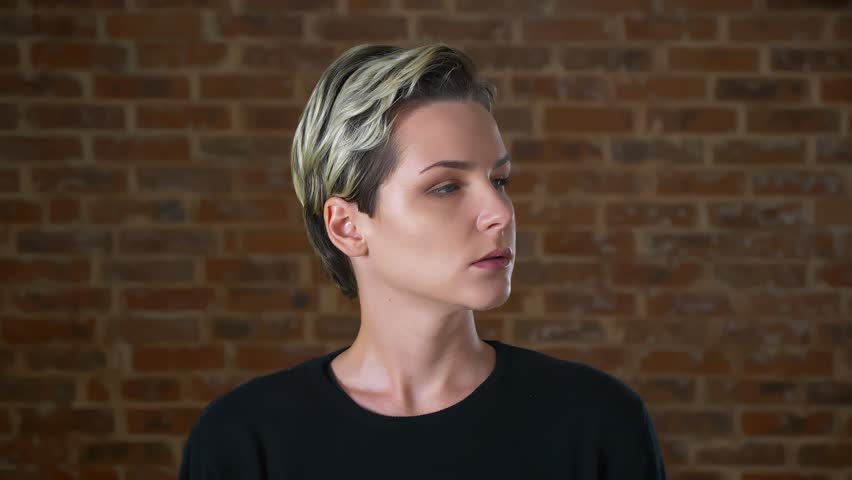 Calm and confident female is turning her head and looking straight at camera with relaxed face and natural posing in red studio