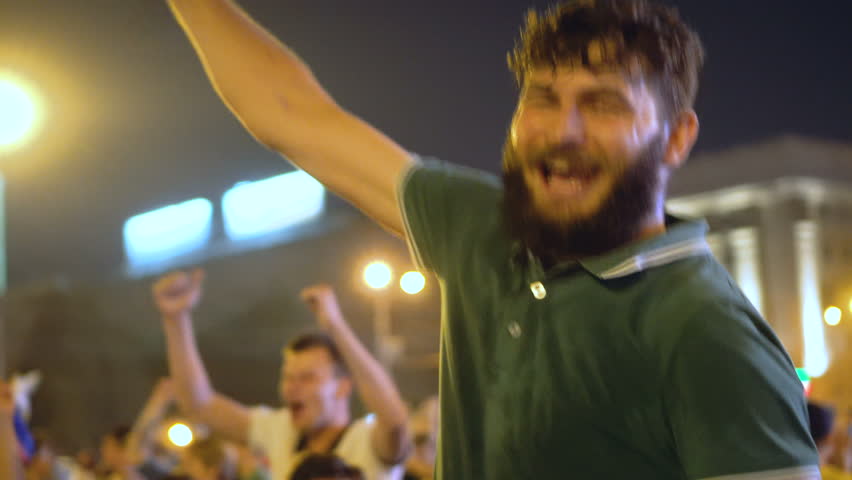 Guy in green T-shirt rejoices at street party in the night city winning football. Atmospheric celebration in honor of victory. Guy goes into crowd jump and rejoices with crowd victory of Russia