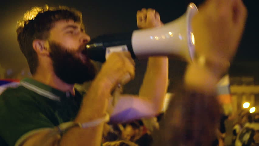 Rebel football fan protester with loudspeaker against current government. Bearded man protests for civil rights. Rioting activist people in night city street, crowd strike, riot person with megaphone. Royalty-Free Stock Footage #1017936994
