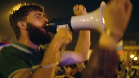 Rebel football fan protester with loudspeaker against current government. Bearded man protests for civil rights. Rioting activist people in night city street, crowd strike, riot person with megaphone.