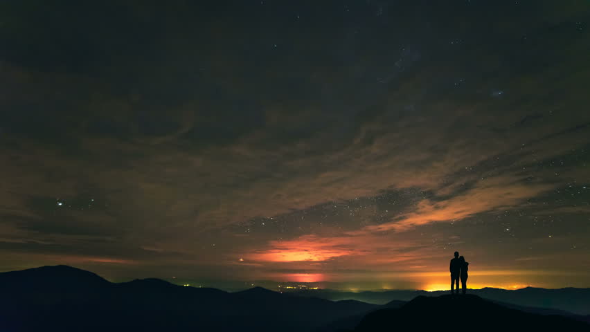 The man and a woman standing on a mountain with stars background. time lapse