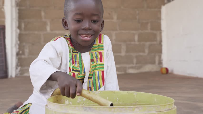 Handsome little African child smiling and playing with a water hose and a bucket. 4K RAW footage - please color grade and stabilize in postproduction.