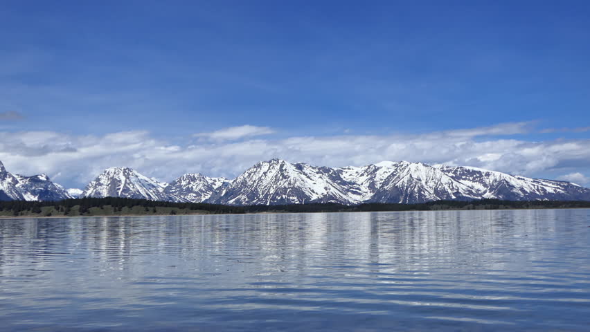 Spectacular Jenny Lake with beautiful snowy mountain peaks across water, rock lands in water creating small waves