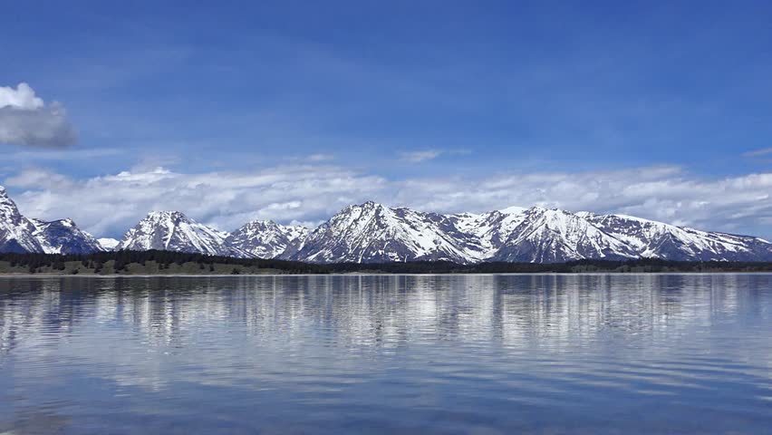 Spectacular Jenny Lake with beautiful snowy mountain peaks across water, rock lands in water creating small waves