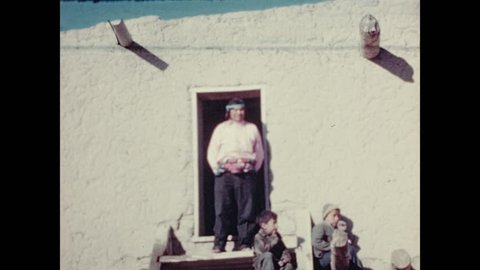 1930s: Men and children at door of adobe home. Native American ceremonial dance. People beat drums.