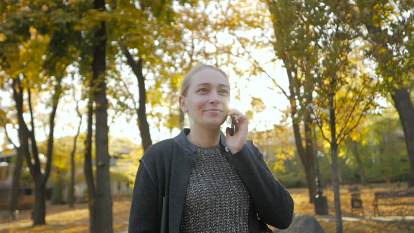 Woman standing in a beautiful autumn park talking on the phone