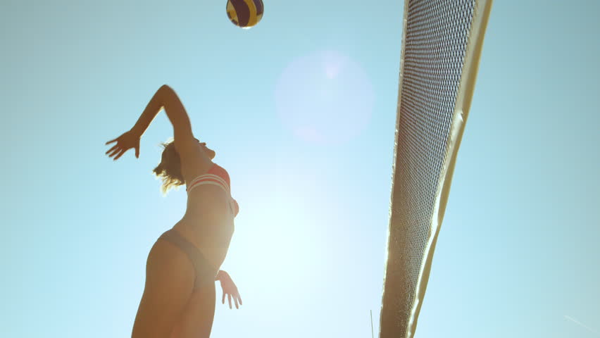 SLOW MOTION, LOW ANGLE, CLOSE UP, LENS FLARE: Athletic female beach volleyball player spikes the ball and scores a point during a competition. Cheerful girl enjoying the summer and playing voleyball.