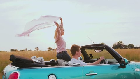 4K side view of a happy young couple out in the country driving in a convertible car