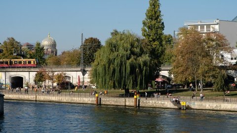 Berlin, Germany - october 2018: People in public park (Monbijoupark) / riverside in Berlin Mitte with trains passing by in background on a sunny summer day 