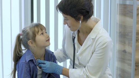 Kind female pediatrician using stethoscope to listen to breath sounds of cute little patient during medical examination in hospital, medium shot