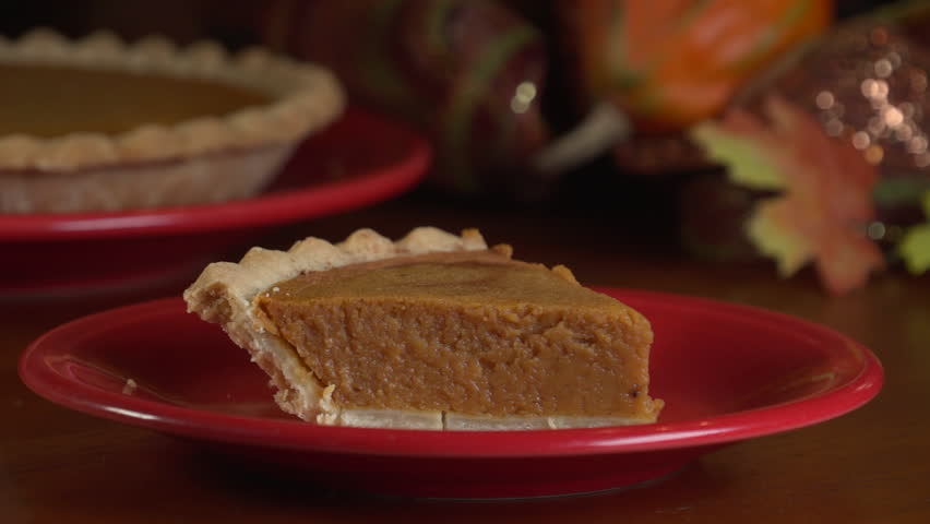 Close up of a slice of pumpkin pie on a red plate, adding a dollop of whipped cream on top