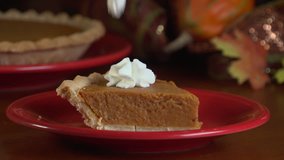 Close up of a slice of pumpkin pie on a red plate, adding a dollop of whipped cream on top - Powered by Shutterstock - Get 15% off with code: PIKWIZARD15