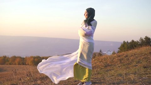 portrait of a stylish girl in a hijab at sunset in the mountains stands on the edge of a cliff