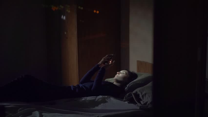 Concept of tracking through the window, the girl lies on the bed and uses the phone | Shutterstock HD Video #1017979996