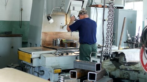 A man specializes a driller drilling holes on a drilling machine in a metal workpiece, a small business, private workshop, bench