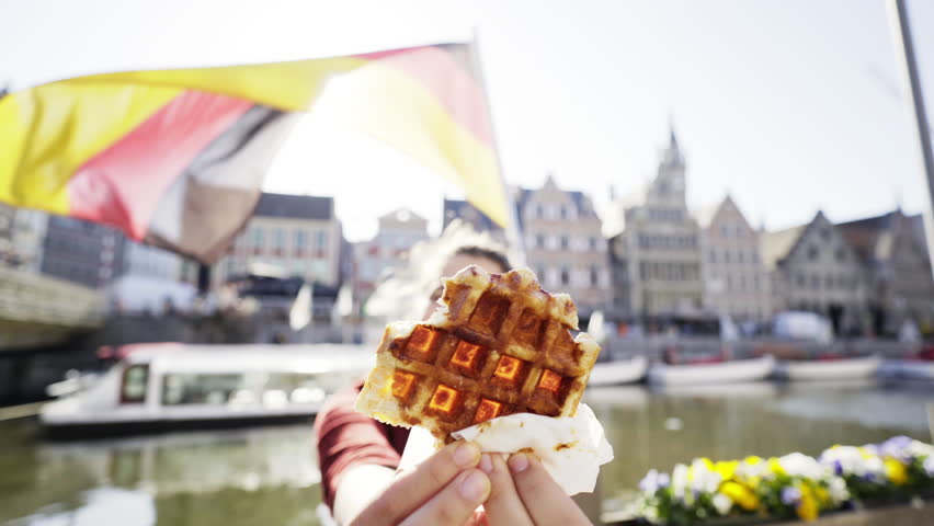 Woman with waffle in european city. Young brunette pull face on camera, have fun with belgian waffle, laughing and happy in sun shine on background of city canal. Ghent, Belgium
