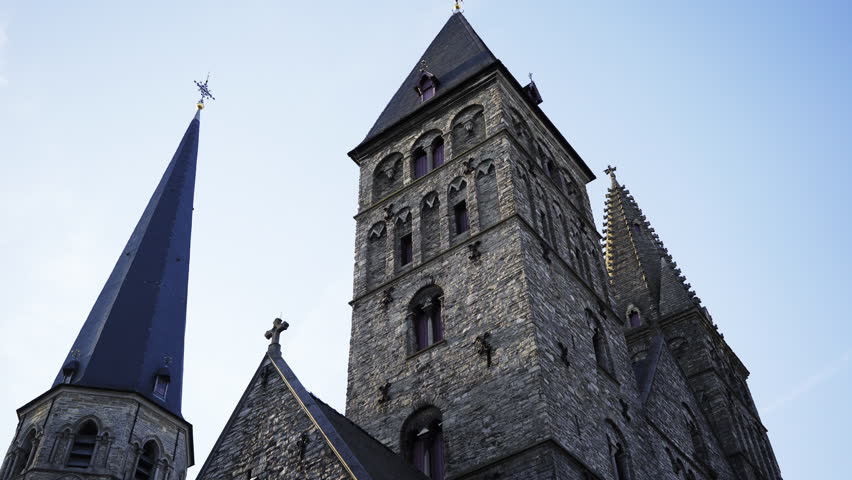 View from bottom to top medieval church in history centre of european city.Circle panoram around one of towers, close-up towers and roofs with cross at blue sky background. Ghent, Belgium