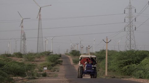 JAISALMER, RAJASTHAN, INDIA - AUG 26: Man driving tractor passes wind turbines on August 26, 2018 in Jaisalmer, Rajasthan, India