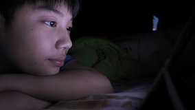 Young asian boy playing with a cellphone or smartphone on a bed. night