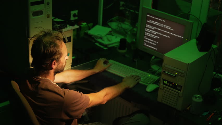 Adult hacker works with old software on retro computers with blue screen and dark green lighting