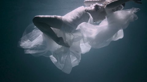 Young woman under the water, she is wearing a white dress.
