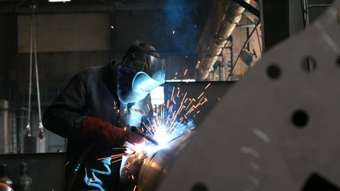 Professional worker welding metal on plant