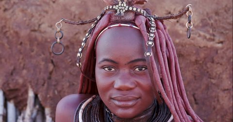 4K close-up portrait view of a pretty Himba girl showing head gear and neck jewellery, and looking into camera,Namibia
