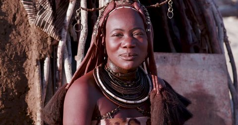 4K close-up portrait view of a pretty Himba girl showing head gear and neck jewellery looking straight into the camera,Namibia