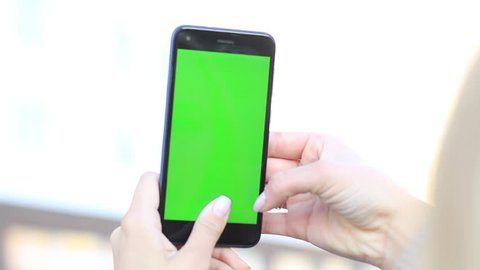 girl's hands holding a mobile phone with a green screen.