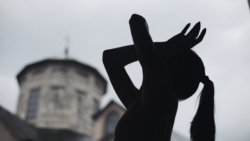 Young professional female dancer is performing acrobatic dance along the medieval street under the rain. Ballerina dancing in water drops, slow motion