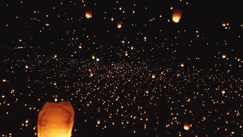 Drone footage of thousands of glowing lanterns flying across screen. Beautiful floating lanterns light the night sky as thousands of people gather to let their wishes fly.
