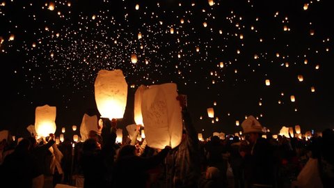 Thousands of lanterns float in the night sky in slow motion. Huge gathering of people light lanterns with flames. 
